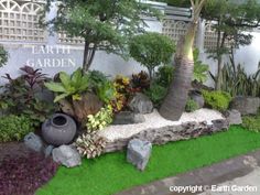 a garden with rocks and plants in front of a white wall that says earth's garden