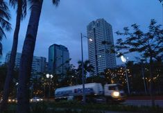 a truck driving down a street next to tall buildings and palm trees in the evening