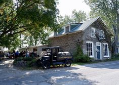 an old fashioned truck parked in front of a stone building with people standing outside it