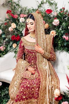 a woman in a red and gold bridal gown sitting on a white couch with flowers behind her