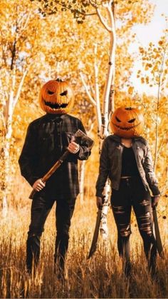 two people wearing pumpkin hats and holding axes in the woods with trees behind them,