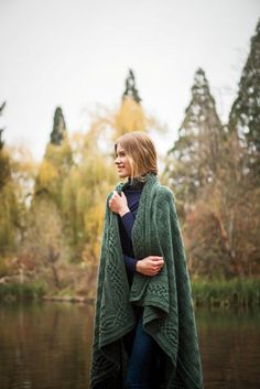 a woman standing in front of a body of water wearing a green cardigan sweater