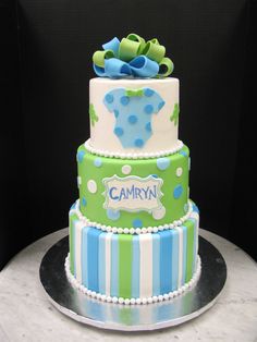 a three tiered cake is decorated with blue and green stripes, polka dots and bows