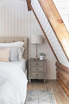 an attic bedroom with white walls and wood flooring, a bed has two pillows on it