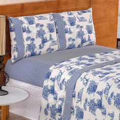 a bed with blue and white bedspreads on it, next to a night stand