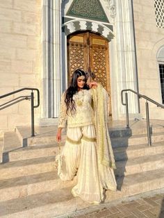 a woman in a white outfit is standing on the steps outside an ornately decorated building