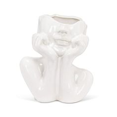 a white ceramic vase with a face and hands on it's sides, sitting in front of a white background