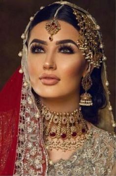 a woman wearing a red and gold bridal outfit with jewelry on her head, in front of a brown background