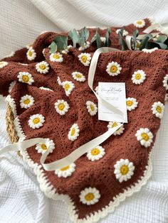 a crocheted blanket with daisies on it and a white ribbon around the edge