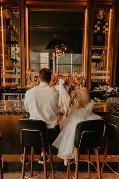 a man and woman sitting at a bar with their back to the camera, facing each other