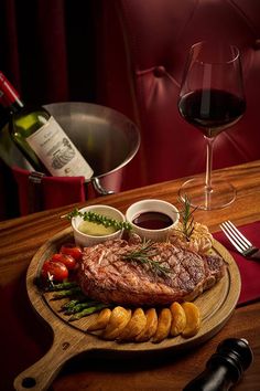 a steak and some vegetables on a wooden platter next to a glass of wine