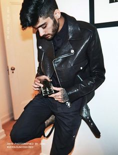 a man in a black leather jacket leaning on a white wall with the words versus