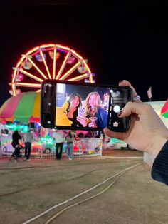 a person holding up a cell phone in front of a carnival