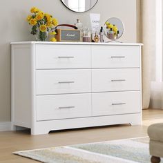 a white dresser with yellow flowers on top and a round mirror above it, in a living room