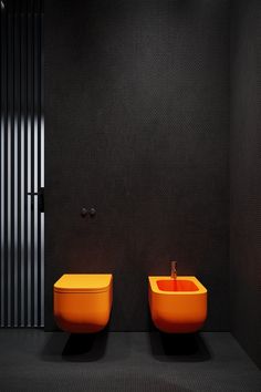 two orange sinks sitting next to each other on a black floor in a room with dark walls