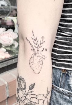 a woman's arm with flowers and a heart tattoo on the left side of her arm