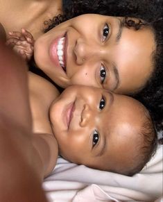 two young children laying on top of a white bed next to each other and smiling at the camera