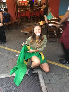 a woman sitting on the ground with her mouth open and holding a green cloth in front of her face