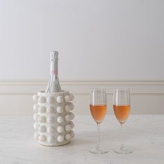 two wine glasses and a bottle on a marble counter top with white walls in the background