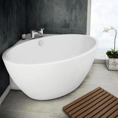 a white bath tub sitting on top of a bathroom floor next to a wooden mat