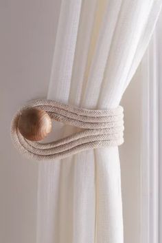 a white curtain with a knot on it and a wooden button hanging from the side