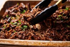 someone is scooping up some shredded meat into a dish with tongs and garnishes