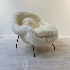 a white chair sitting on top of a hard wood floor covered in sheepskin and metal legs