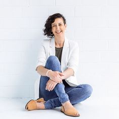 a woman sitting on the floor with her legs crossed and smiling at the camera,