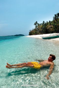 a man laying on his back in the clear blue water near an island with palm trees