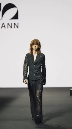 a woman is walking down the runway wearing black pants and a jacket with lace on it