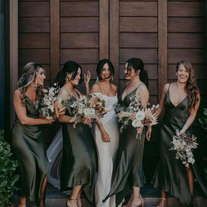 a group of women standing next to each other in front of a wooden door holding bouquets