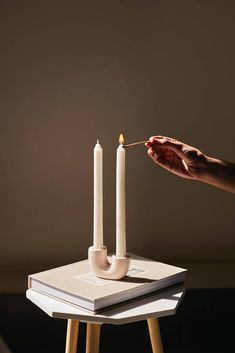 a person lighting a candle on top of a book next to a pair of candles