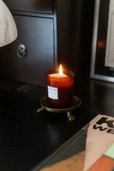 a lit candle sitting on top of a black table next to a lamp and some papers