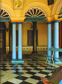 a person sitting on a bench in a room with blue pillars and arches, looking at something