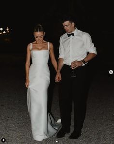 a man and woman in formal wear holding hands while standing next to each other at night