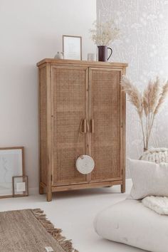 a wicker cabinet in the corner of a room next to a white couch and pillows