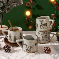 three mugs on a table with pine cones and christmas decorations