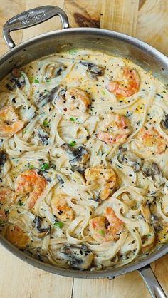 a pan filled with pasta and shrimp on top of a wooden table