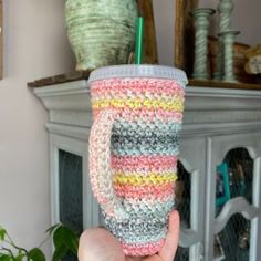 a hand holding a cup with a straw in it and a crocheted lid