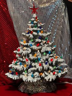 a small white christmas tree sitting on top of a red cloth covered table next to a curtain