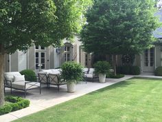 an outdoor patio with chairs and tables surrounded by trees in front of a house on a sunny day