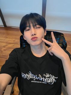 a young man sitting in a chair making the peace sign with his hand while wearing a black shirt