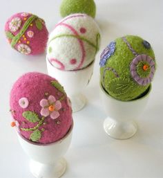 four different types of felted balls on display in white vases with pink flowers and green leaves