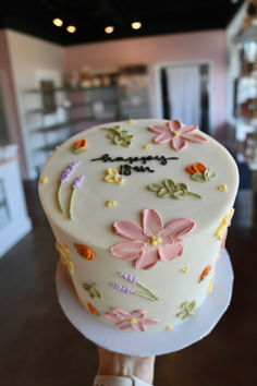 a cake with flowers on it is being held by a woman's hand in front of the camera