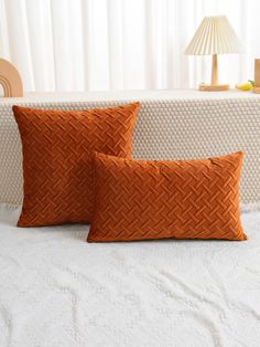 two orange pillows sitting on top of a bed next to a white blanket and lamp