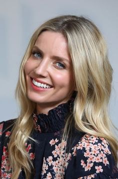 a woman with long blonde hair and blue eyes smiles at the camera while wearing a floral blouse