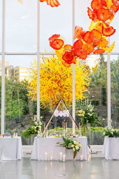 a room filled with lots of tables covered in white linens and tall glass windows