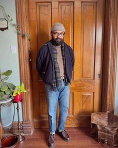 a man standing in front of a wooden door wearing glasses and a hat with his hands on his hips