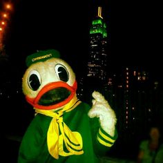 a person dressed in a green shirt and yellow scarf standing next to a tall building