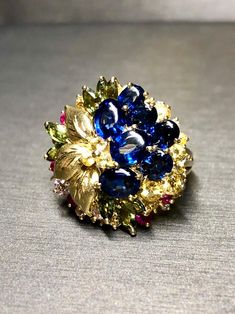 A colorful cocktail ring crafted in deep 18K yellow, gold and set with approximately 7.50cttw in oval buff top blue sapphires as well as round yellow and pink sapphires as well as green marquise shaped sapphires and .15cttw in G-I color Vs1-2 clarity round diamonds. Dimensions/Weight: Ring measures .90" in diameter and weighs 13.9g. Size 7.5 (sizable). Condition: All stones are secure and in perfectly wearable condition. R-BCCL Luxury Gold Sapphire Ring Collectible, Luxury Gold Multi-stone Sapphire Ring, Luxury Multicolor Sapphire Ring For Formal Occasions, Multicolor Sapphire Ring In Fine Jewelry Style, Multicolor Sapphire Multi-stone Ring, Multicolor Multi-stone Sapphire Ring, Multicolor Sapphire Gemstone Ring, Oval Blue Multi-stone Sapphire Ring, Multicolor Oval Sapphire Ring